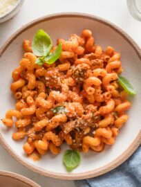 Pasta with crumbled sausage in a creamy tomato sauce, topped with fresh basil leaves and grated Parmesan cheese.