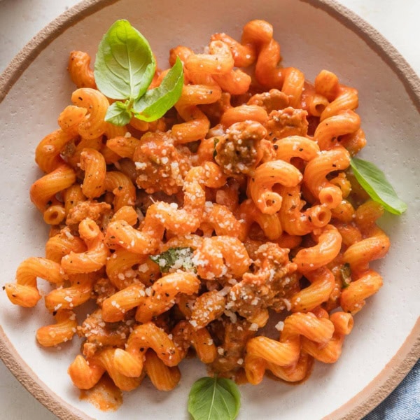 Pasta with crumbled sausage in a creamy tomato sauce, topped with fresh basil leaves and grated Parmesan cheese.