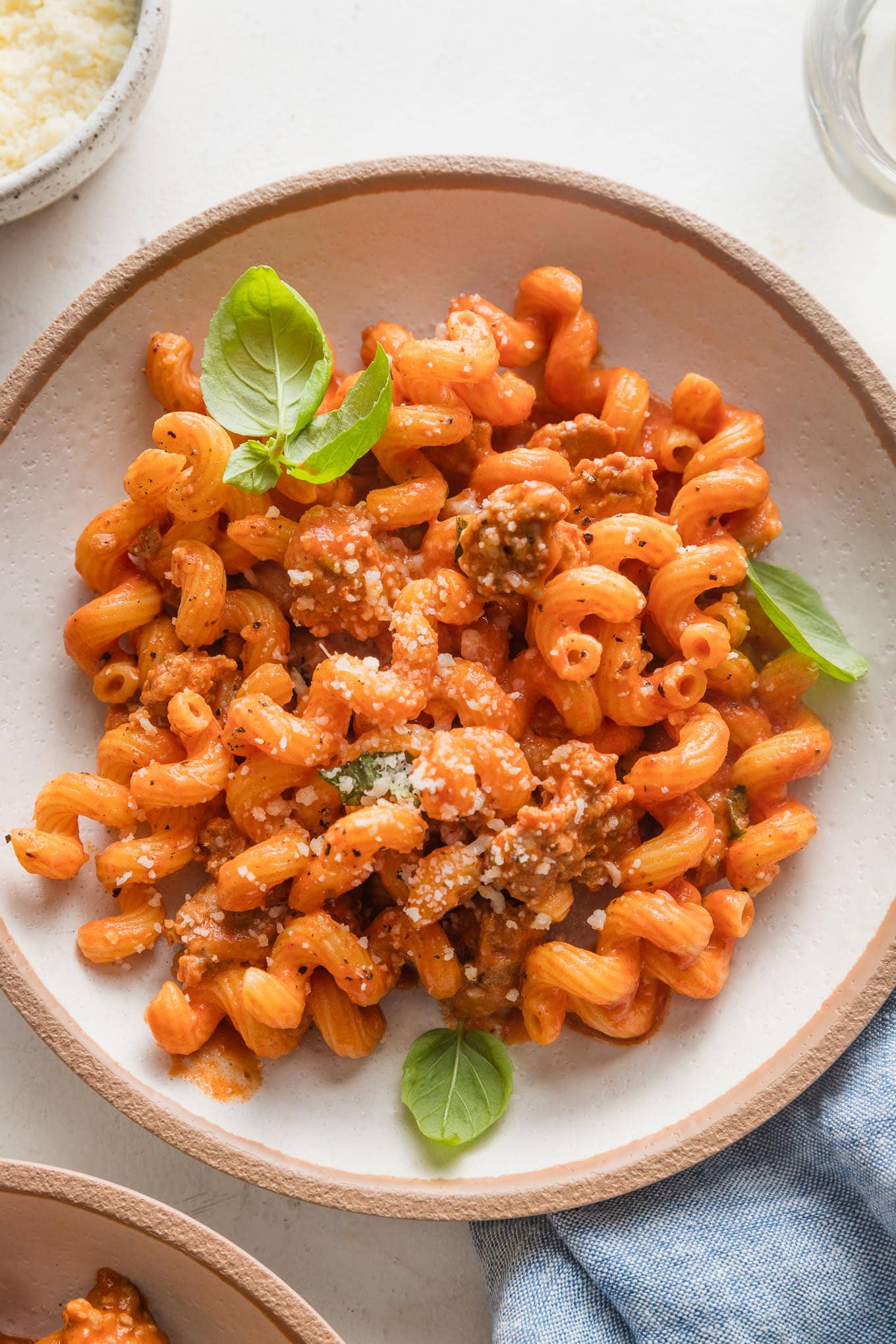 Pasta with crumbled sausage in a creamy tomato sauce, topped with fresh basil leaves and grated Parmesan cheese.