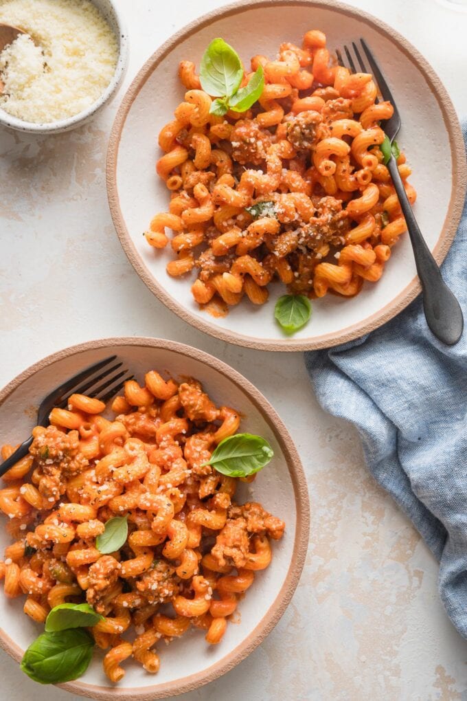 Table set with two bowls of creamy tomato sausage pasta and extra Parmesan.