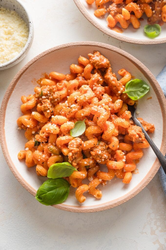 Shallow pasta bowl full of creamy tomato sausage pasta garnished with fresh basil and Parmesan.