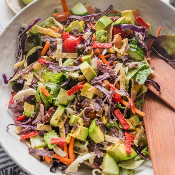 Large white ceramic bowl full of an easy Mexican salad with avocado, cabbage, peppers, tortilla strips, and a red wine vinaigrette.