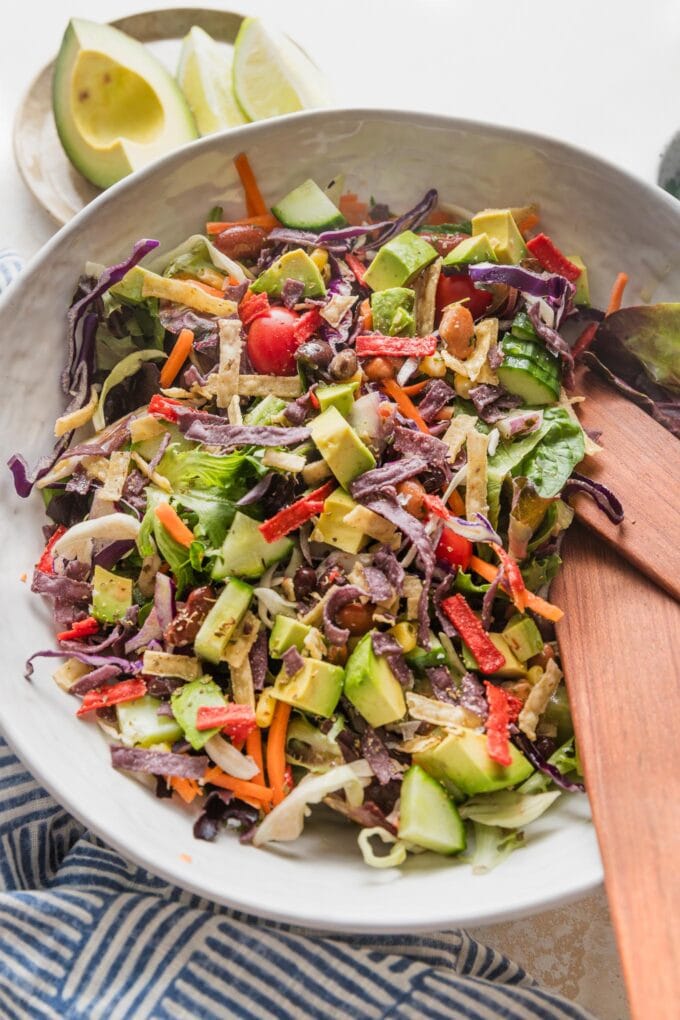 Large white ceramic bowl full of an easy Mexican salad with avocado, cabbage, peppers, tortilla strips, and a red wine vinaigrette.