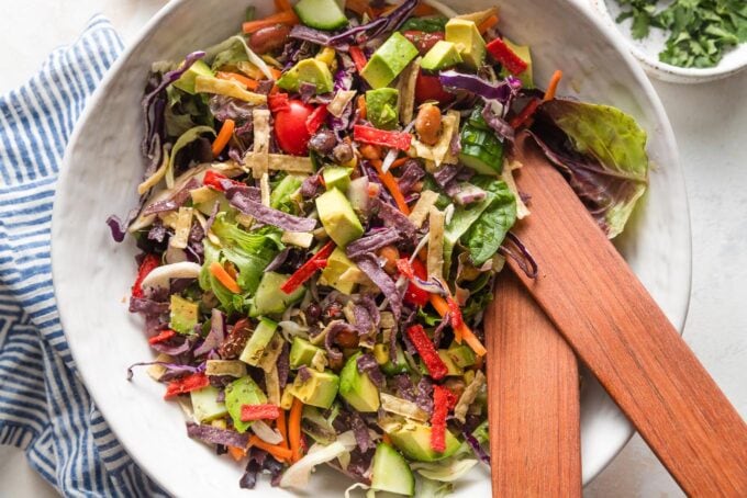 Close up landscape-oriented photo of an easy Mexican salad being tossed by wooden salad tongs in a large bowl.