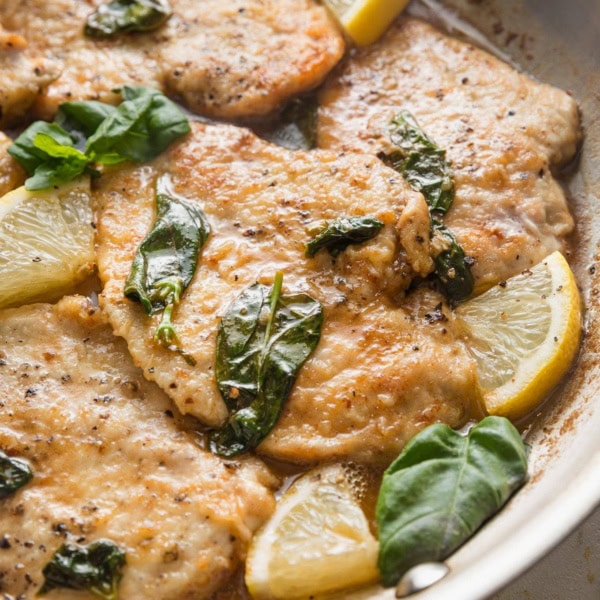Angled view of a golden brown chicken breast dressed in a buttery basil-infused lemon sauce.