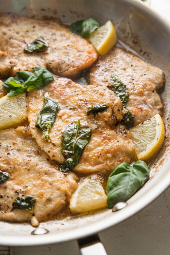 Angled view of a golden brown chicken breast dressed in a buttery basil-infused lemon sauce.