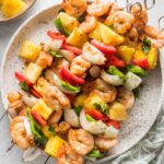 Large white plate filled with shrimp pineapple skewers with sweet onion and chopped bell peppers.