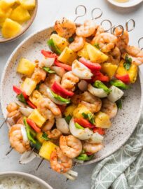 Large white plate filled with shrimp pineapple skewers with sweet onion and chopped bell peppers.