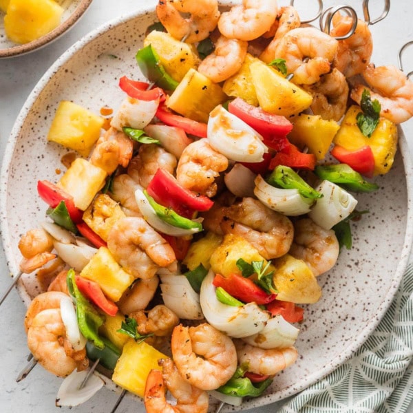 Large white plate filled with shrimp pineapple skewers with sweet onion and chopped bell peppers.