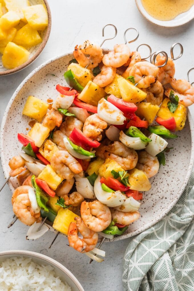 Large white plate filled with shrimp pineapple skewers with sweet onion and chopped bell peppers.