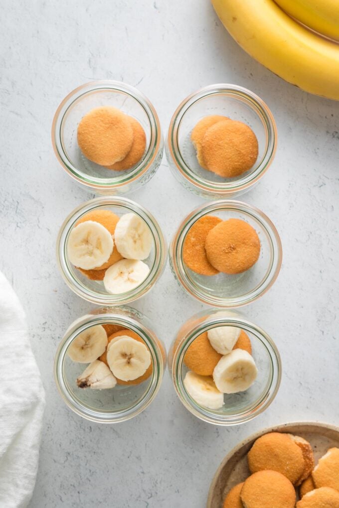 Small tulip glass jars with Nilla wafers and sliced bananas across the bottom.