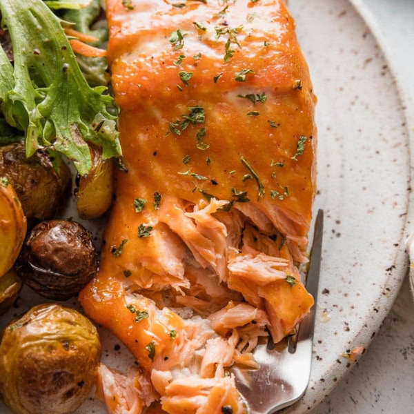 Close up of a brown sugar glazed salmon fillet, with a fork pulling off flaky pieces.