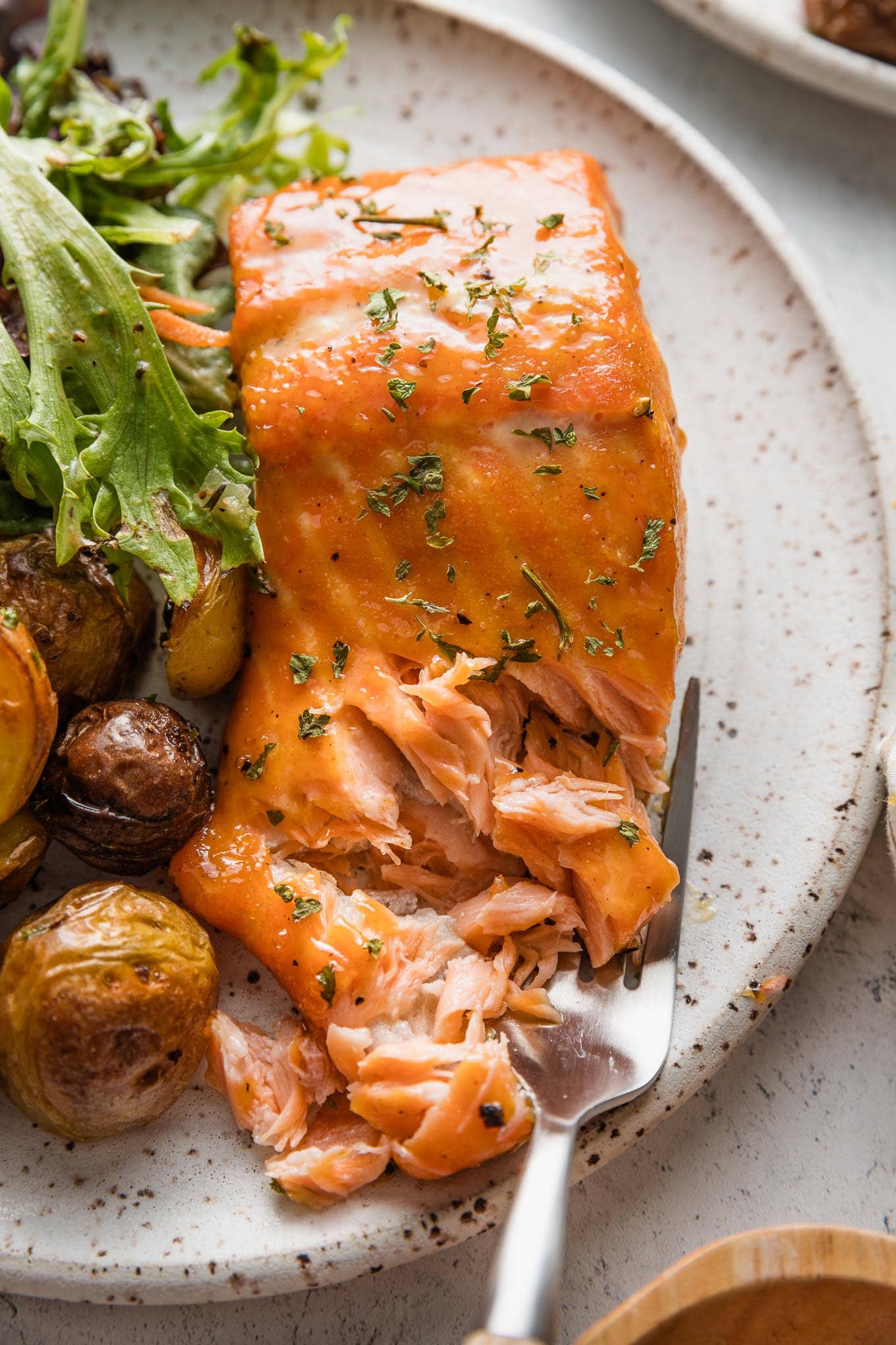 Close up of a brown sugar glazed salmon fillet, with a fork pulling off flaky pieces.