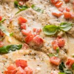 Close up view of a chicken breast with tomato and basil in a light cream sauce.