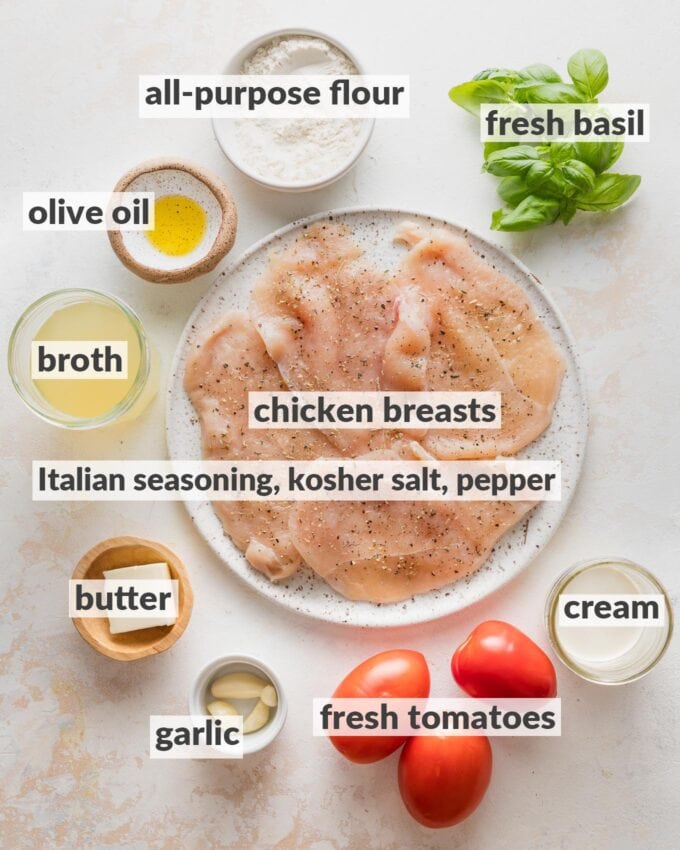 Labeled overhead photo of chicken breasts seasoned with salt, pepper, and Italian seasoning; cream, broth, all-purpose flour, fresh basil, Roma tomatoes, garlic cloves, butter, and olive oil.