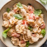 Small bowl filled with a portion of creamy tomato basil tortellini garnished with fresh basil leaves and grated Parmesan cheese.