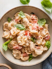 Small bowl filled with a portion of creamy tomato basil tortellini garnished with fresh basil leaves and grated Parmesan cheese.