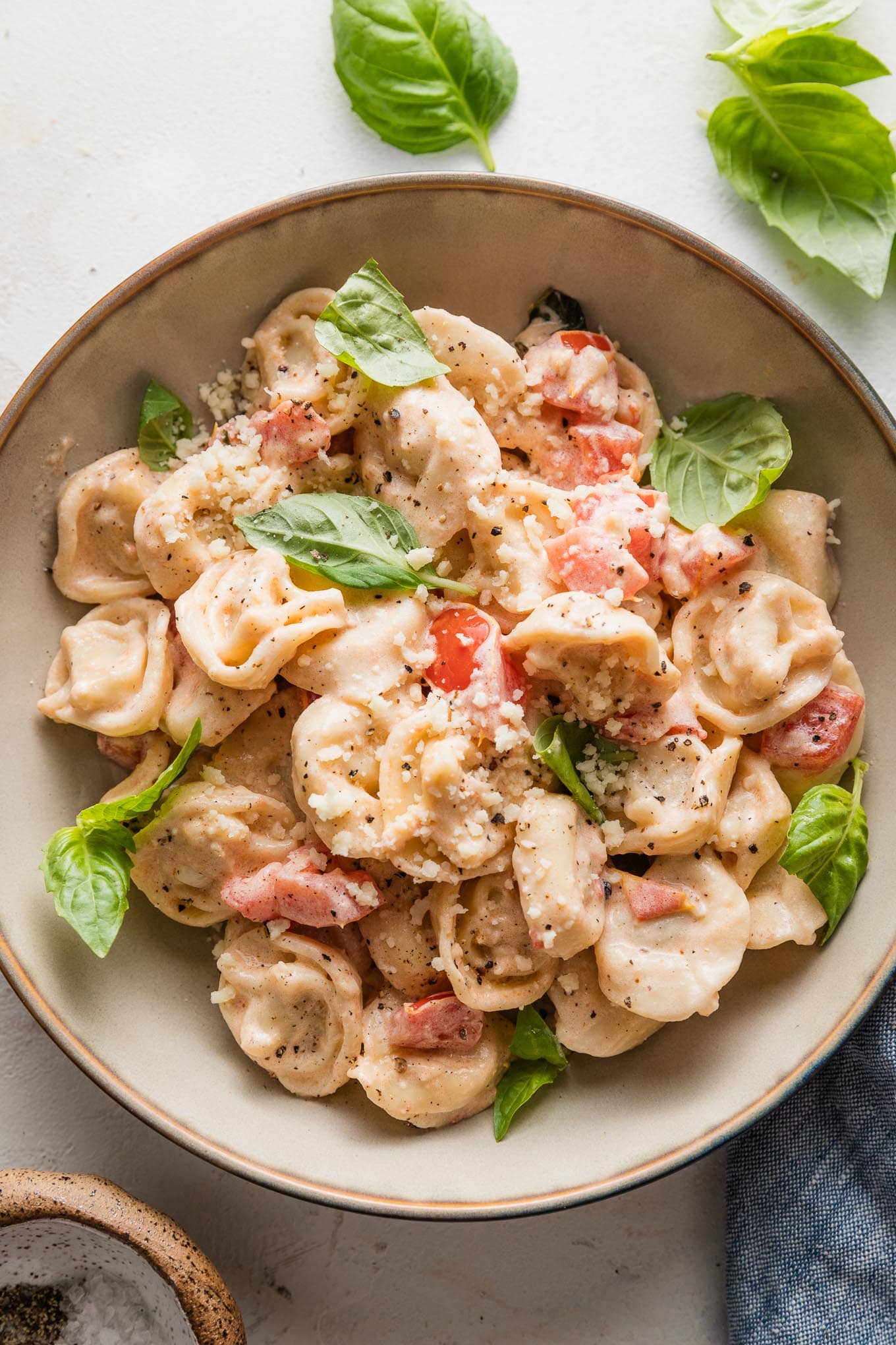 Small bowl filled with a portion of creamy tomato basil tortellini garnished with fresh basil leaves and grated Parmesan cheese.