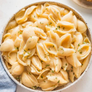 Bowl full of creamy Instant Pot mac and cheese made with small shells and garnished with dried parsley.