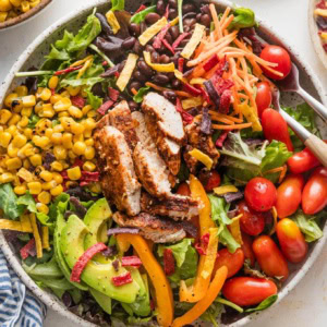 Large bowl filled with a Santa Fe-style salad with grilled chicken, greens, carrot, corn, tomato, avocado, and tortilla strips.