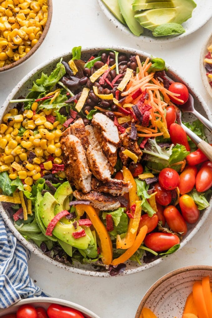 Large bowl filled with a Santa Fe-style salad with grilled chicken, greens, carrot, corn, tomato, avocado, and tortilla strips.