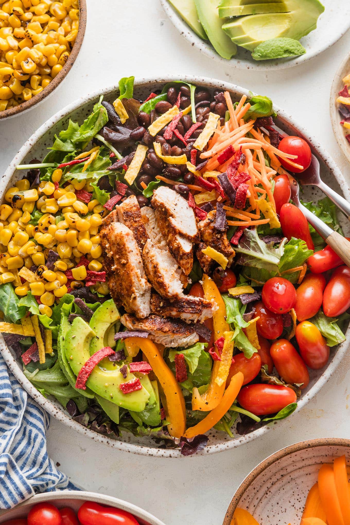 Large bowl filled with a Santa Fe-style salad with grilled chicken, greens, carrot, corn, tomato, avocado, and tortilla strips.