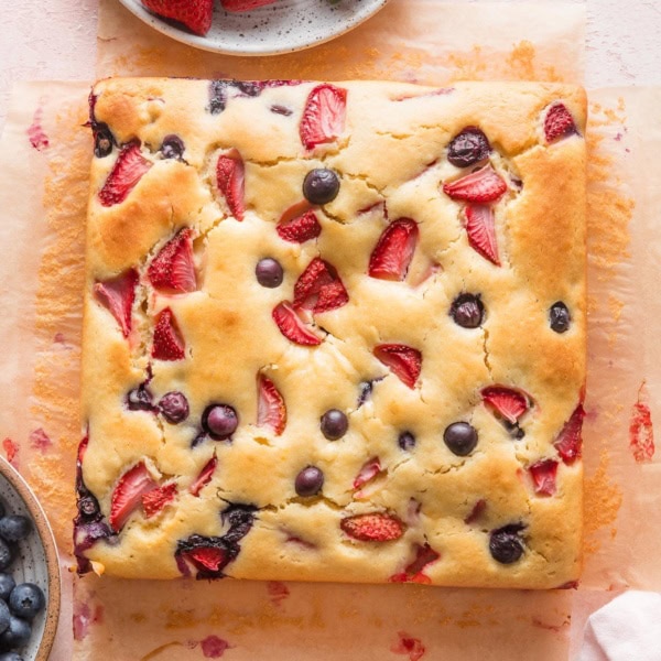Simple strawberry blueberry cake cooling on a light pink countertop.
