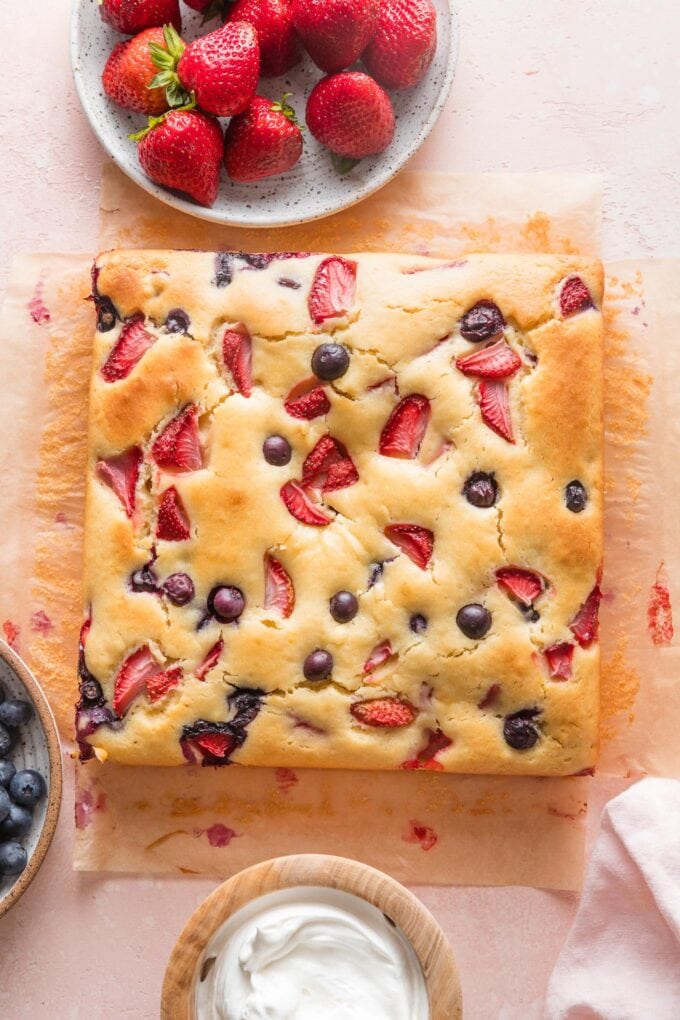 Simple strawberry blueberry cake cooling on a light pink countertop.