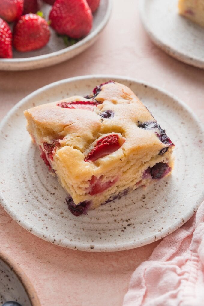 Slice of a light strawberry blueberry cake on a white ceramic plate.