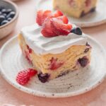 Slice of strawberry blueberry cake topped with whipped cream and extra fresh berries.