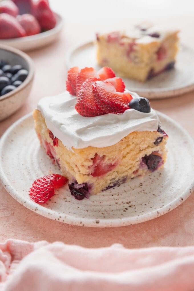 Slice of strawberry blueberry cake topped with whipped cream and extra fresh berries.