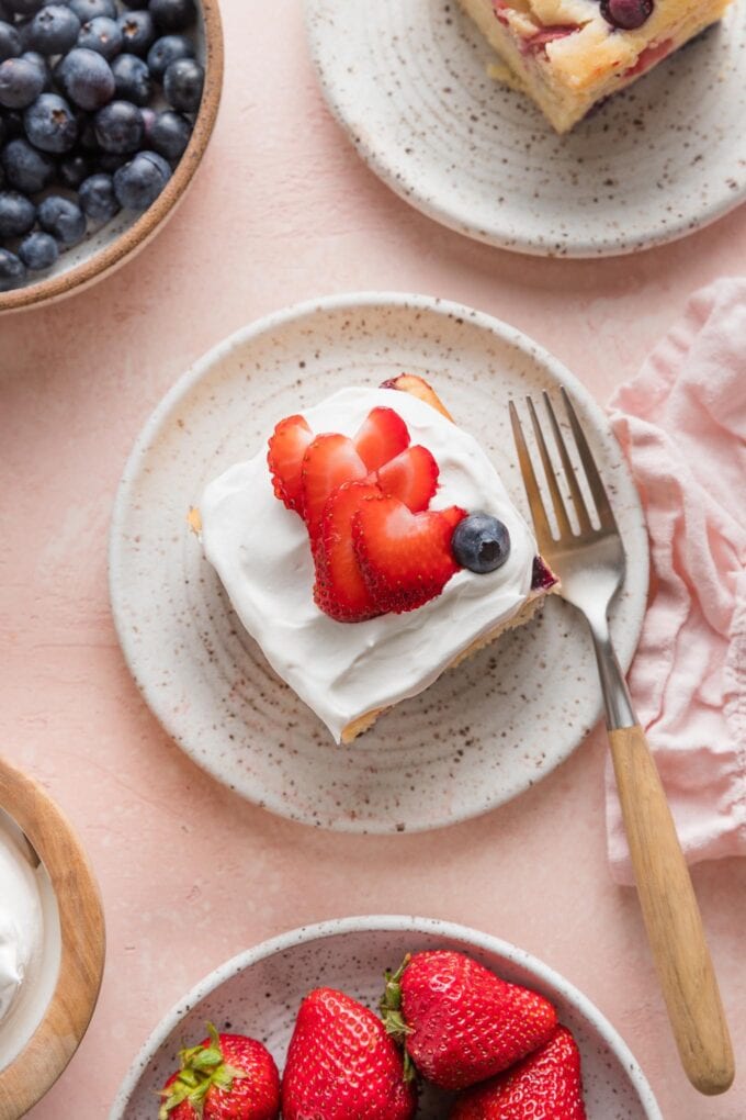Overhead view of small plates filled with a summery strawberry blueberry white cake topped with whipped cream and fresh berries.