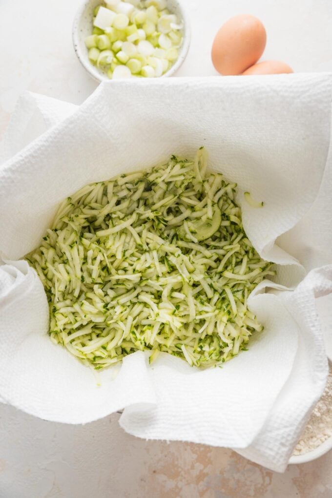 Shredded zucchini drying in a paper towel-lined strainer.