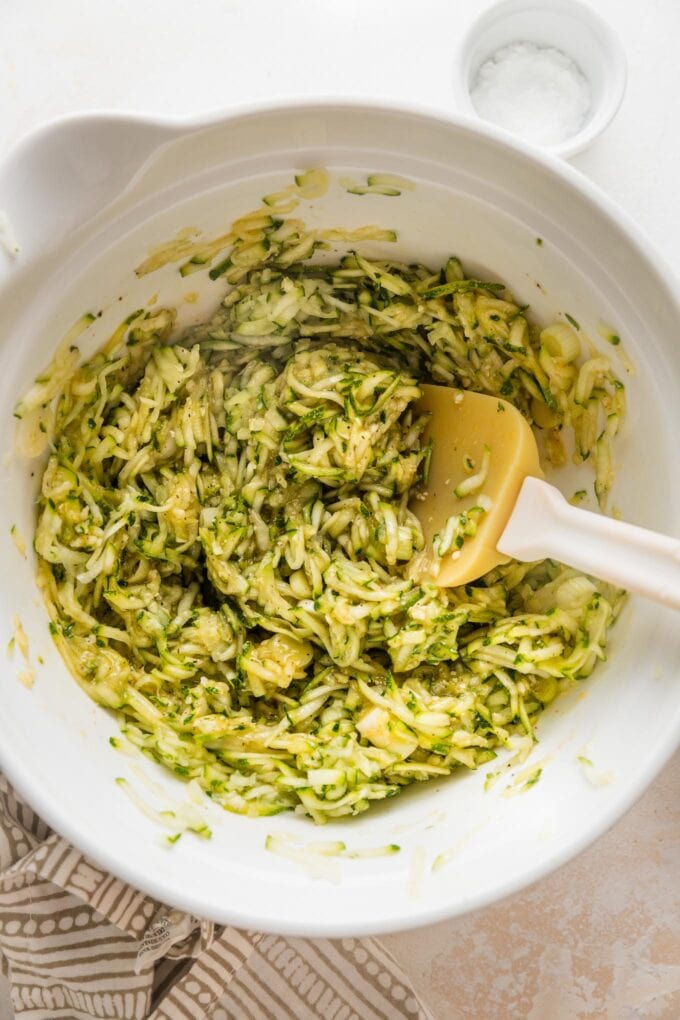 Shredded zucchini added to egg mixture in large white mixing bowl.