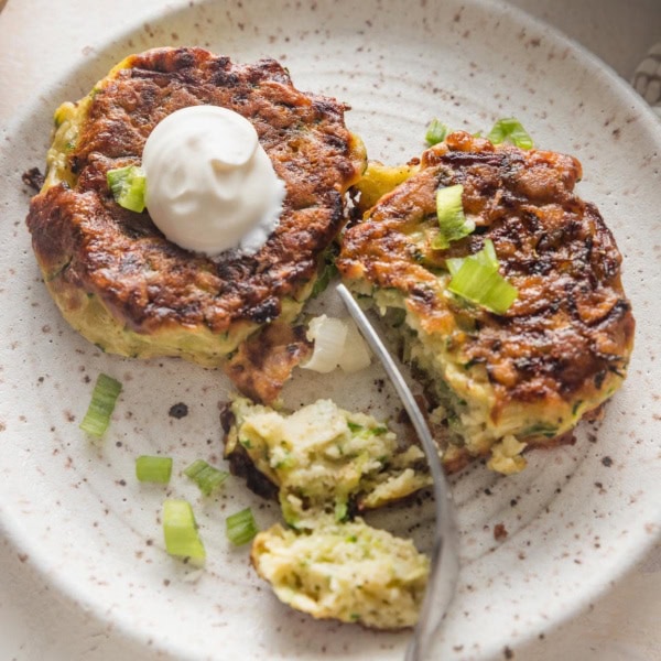 Close up of crispy, golden brown zucchini fritters served on a plate with a dollop of sour cream.