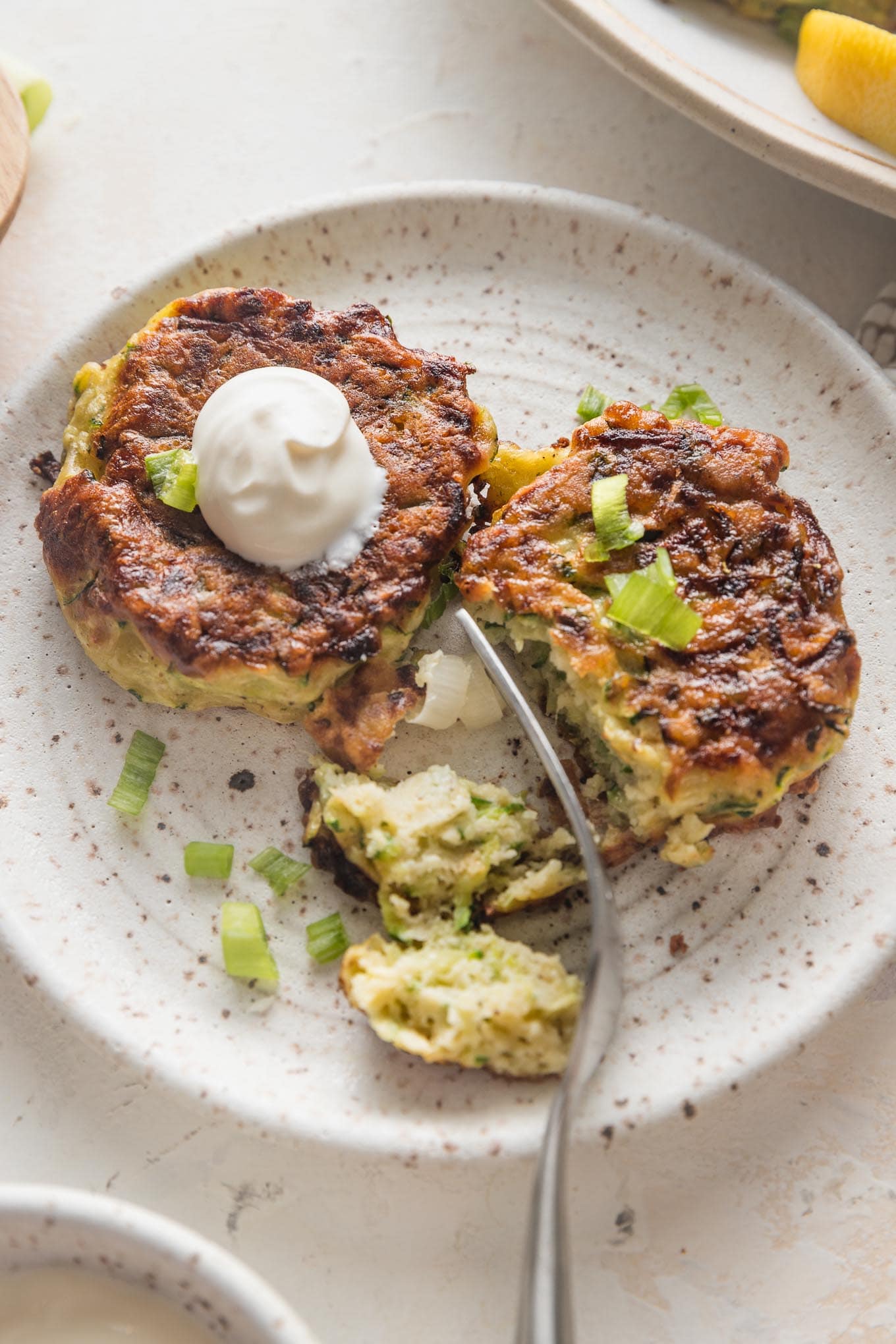 Close up of crispy, golden brown zucchini fritters served on a plate with a dollop of sour cream.