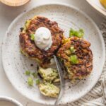 Small plate with two zucchini fritters, one cut into with a fork, the other topped with a dollop of sour cream.