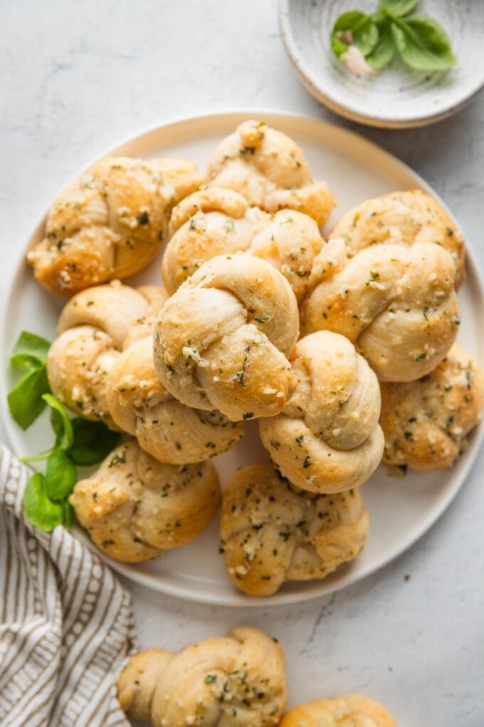 Small white plate piled high with garlic Parmesan biscuit garlic knots with fresh basil scattered nearby.
