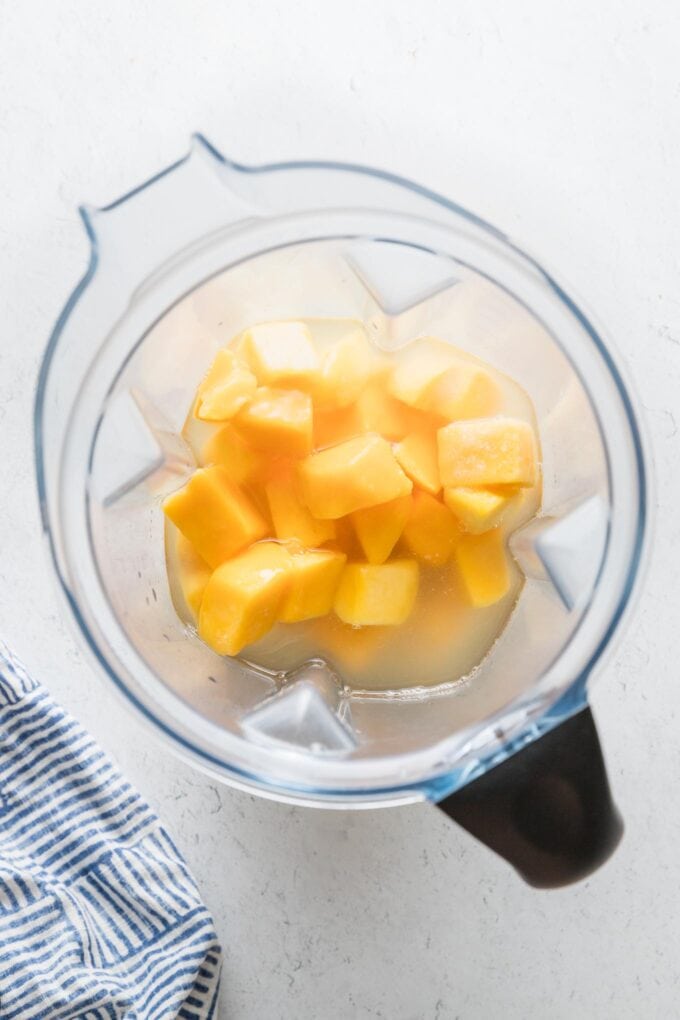 Large blender full of frozen mango chunks, lemon juice, sugar, and water.