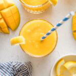 Overhead view of a small glass filled with frozen mango lemonade topped with a lemon wedge and a blue and white striped paper straw.