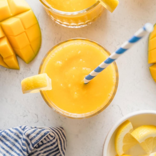 Overhead view of a small glass filled with frozen mango lemonade topped with a lemon wedge and a blue and white striped paper straw.