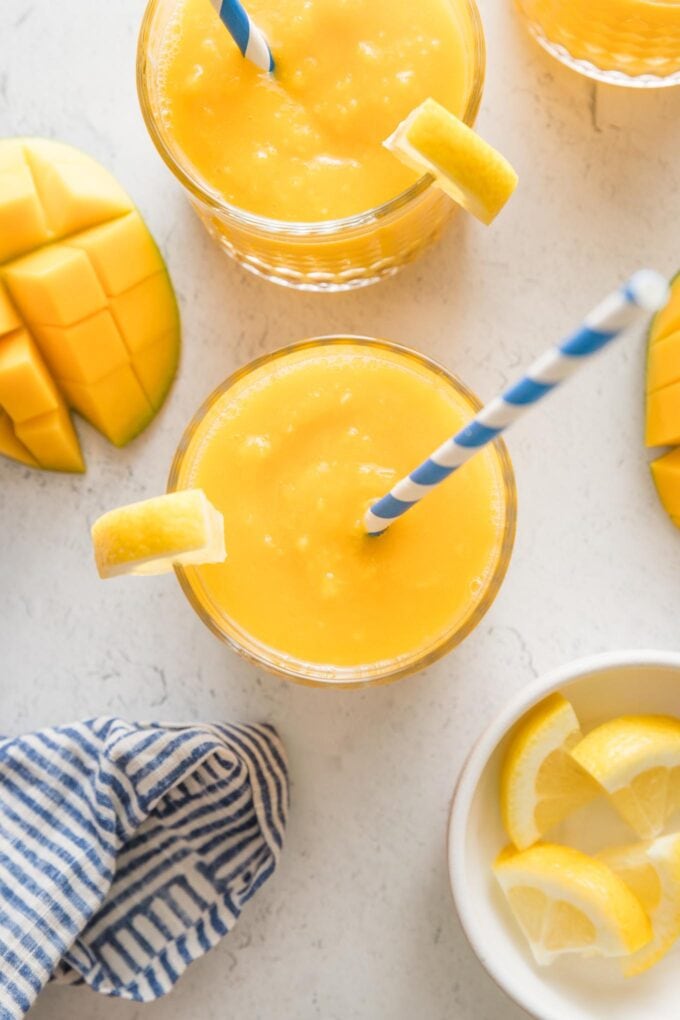 Overhead view of a small glass filled with frozen mango lemonade topped with a lemon wedge and a blue and white striped paper straw.