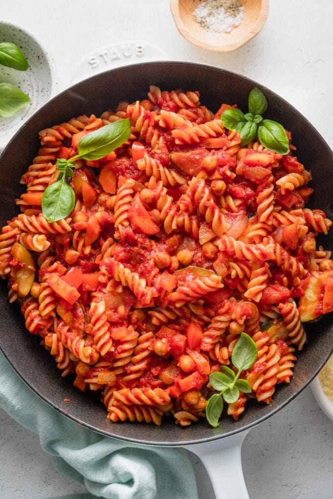 Cast iron skillet filled with a garden vegetable pasta marinara garnished with fresh basil leaves.