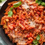 Close up of a garden vegetable pasta with homemade marinara sauce in a skillet garnished with grated Parmesan and fresh basil leaves.
