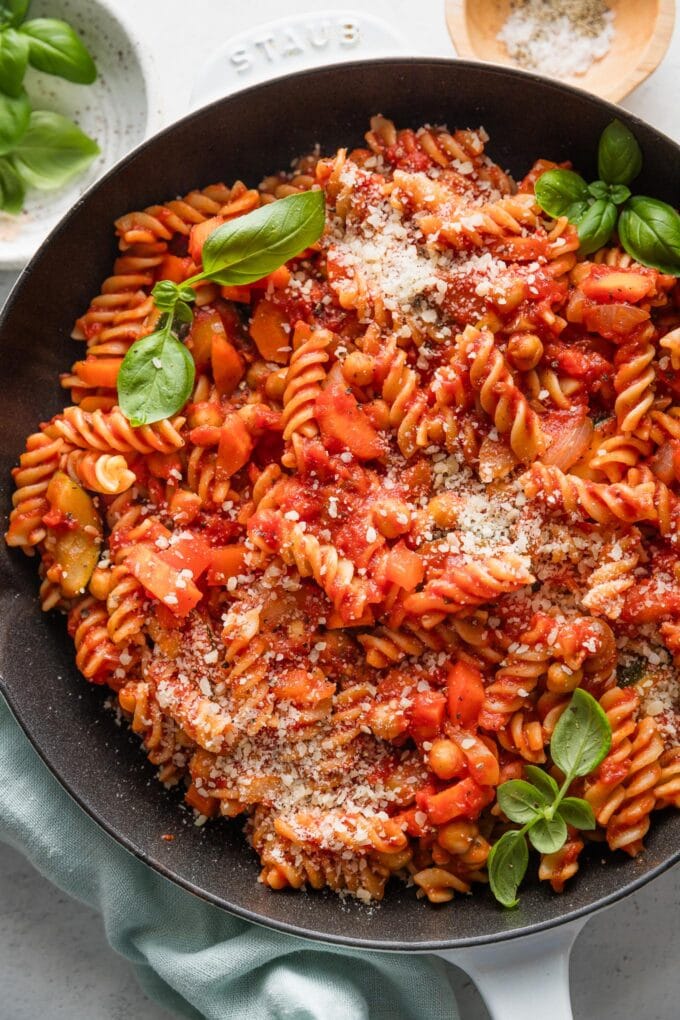 Close up of a garden vegetable pasta with homemade marinara sauce in a skillet garnished with grated Parmesan and fresh basil leaves.