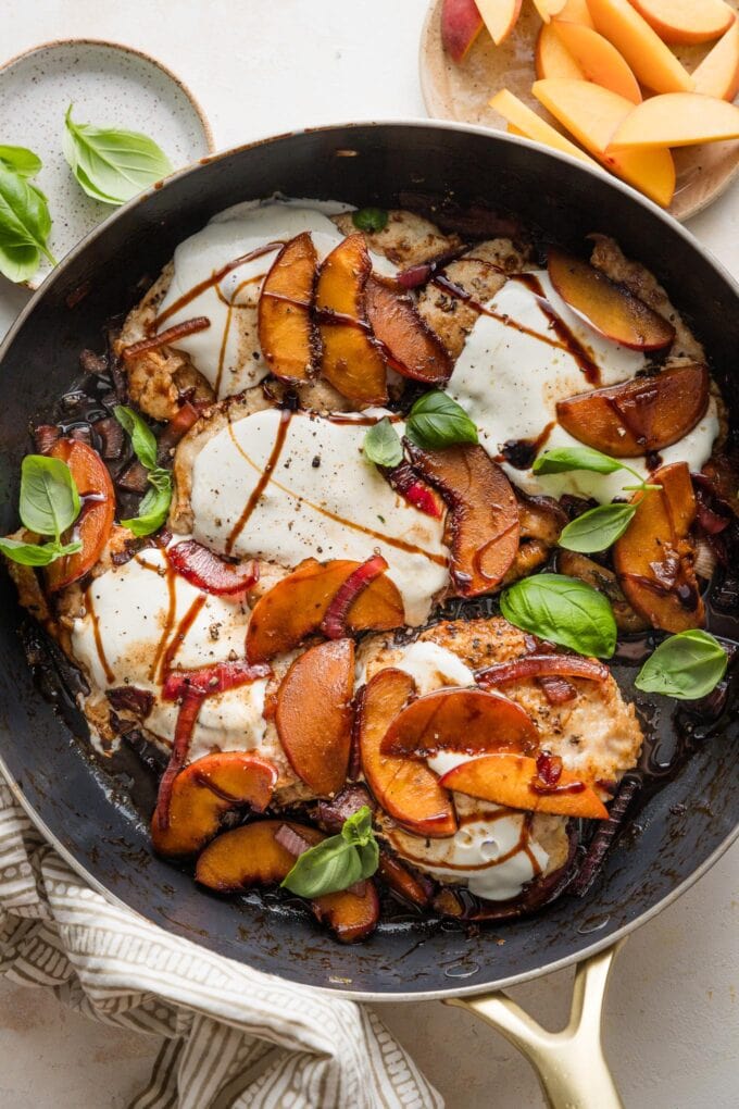Large skillet of peach mozzarella chicken with balsamic, onions, and fresh basil.