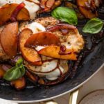 Close up of a pan-seared chicken breast with fresh peaches, mozzarella, basil, and a balsamic glaze.