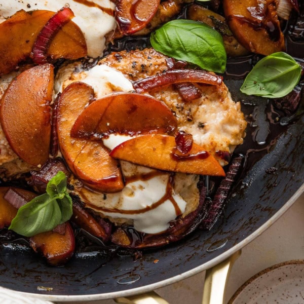 Close up of a pan-seared chicken breast with fresh peaches, mozzarella, basil, and a balsamic glaze.