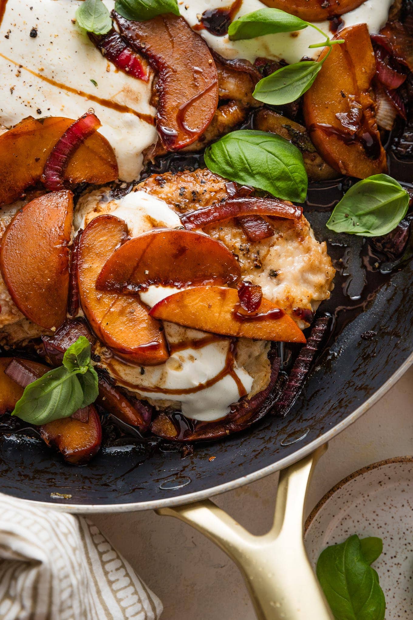 Close up of a pan-seared chicken breast with fresh peaches, mozzarella, basil, and a balsamic glaze.