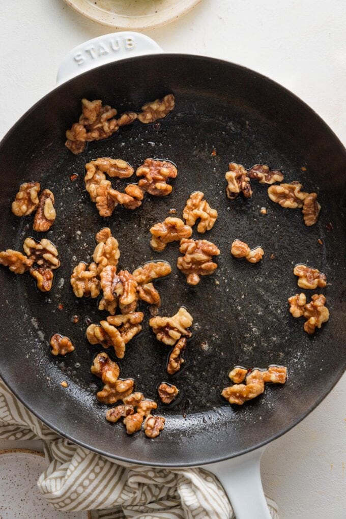 Walnuts toasting in a skillet with lemon zest and red pepper flakes.